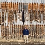 man posing with various pelts on wall